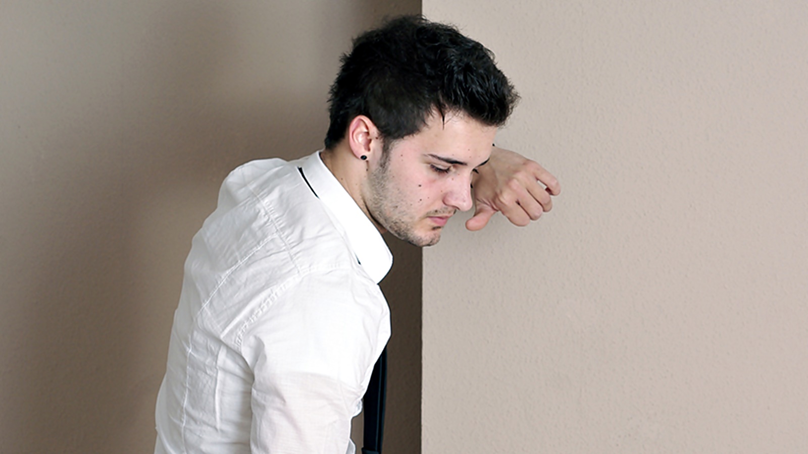 Junger Mann im Anzug lehnt sich erschöpft an eine Wand.