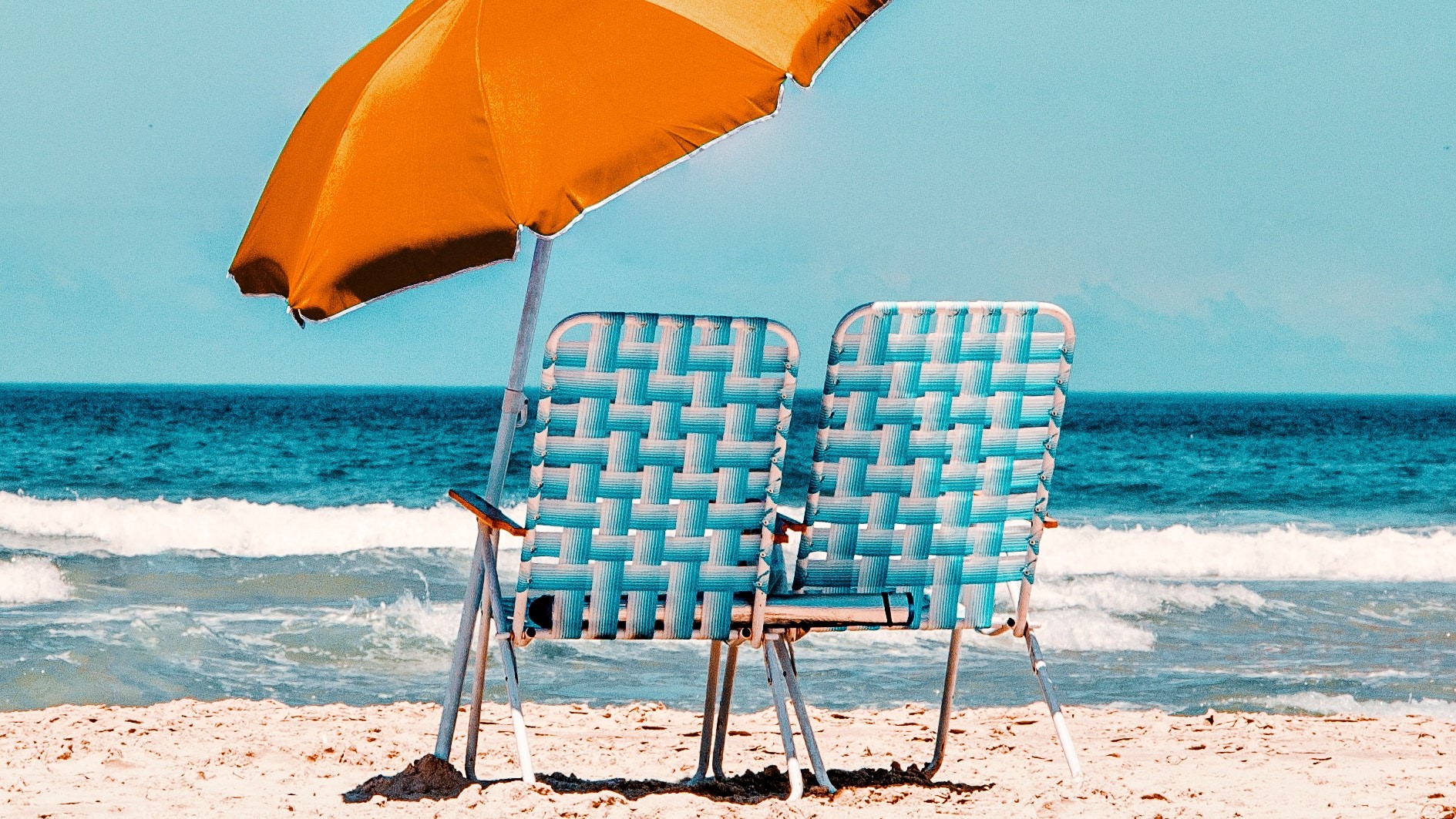 Sonnenschirm orange mit zwei Stühlen am Strand