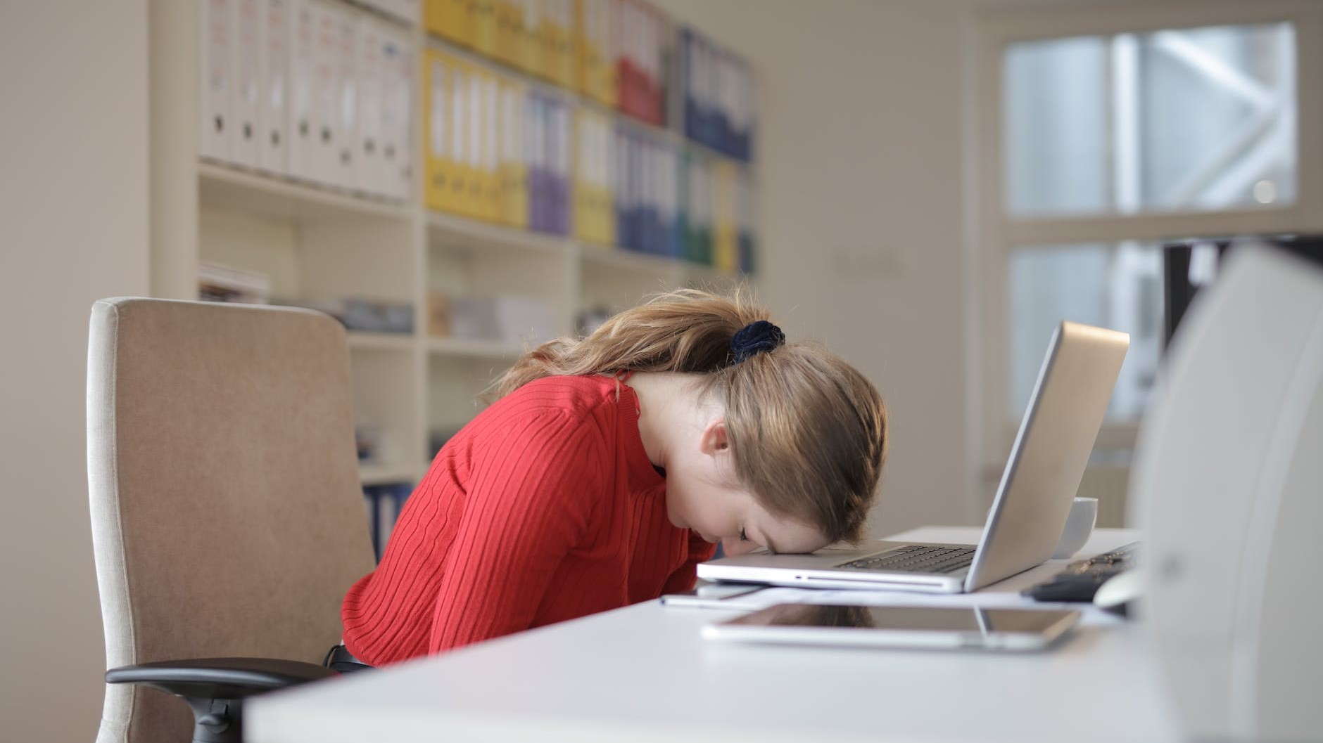 Junge, erschöpfte Frau legt ihren Kopf auf dem Notebook vor sich ab.