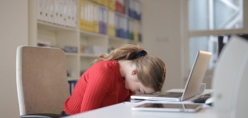 Junge, erschöpfte Frau legt ihren Kopf auf dem Notebook vor sich ab.