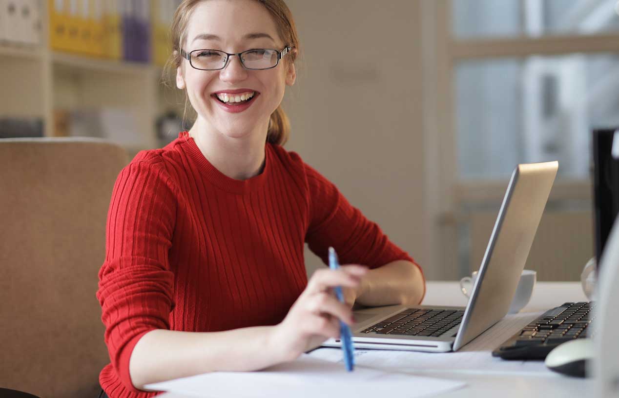 Person vor Laptop an einem Tisch schaut lächend in die Kamera / Pexels