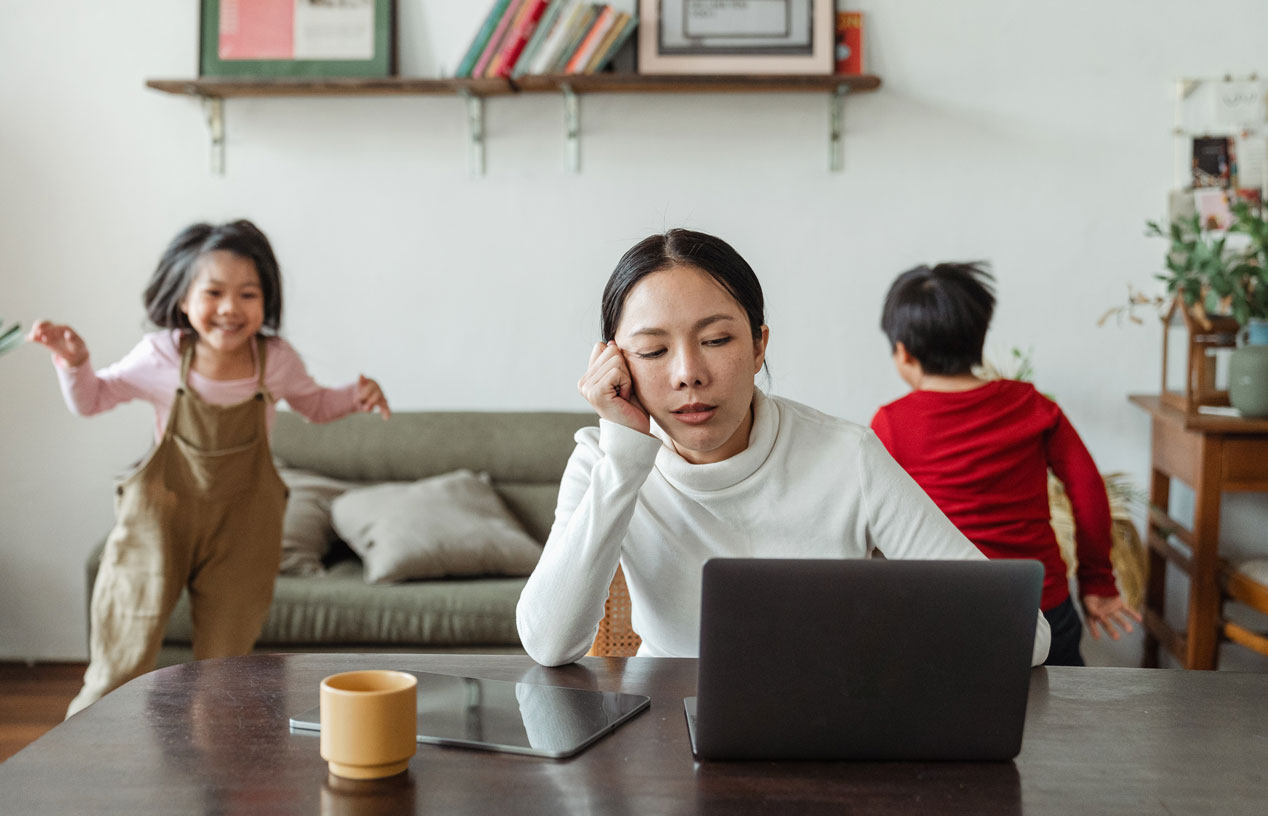 Eine Person am Laptop, mehrere Kinder spielen im Hintergrund / Pexels